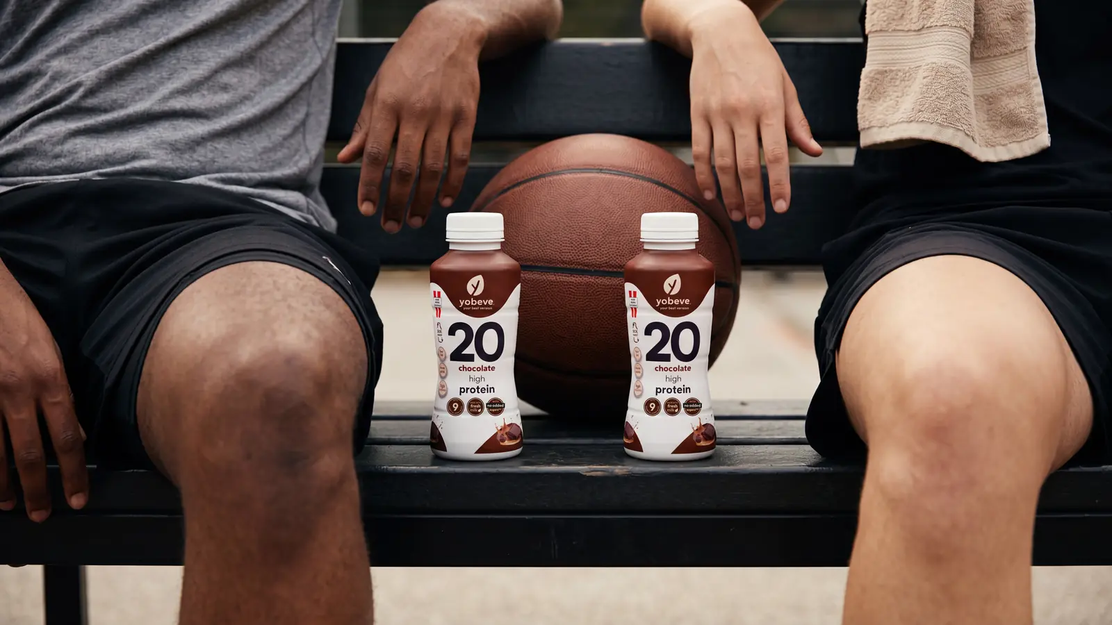 Two athletes seated with yobeve chocolate protein drink bottles beside a basketball